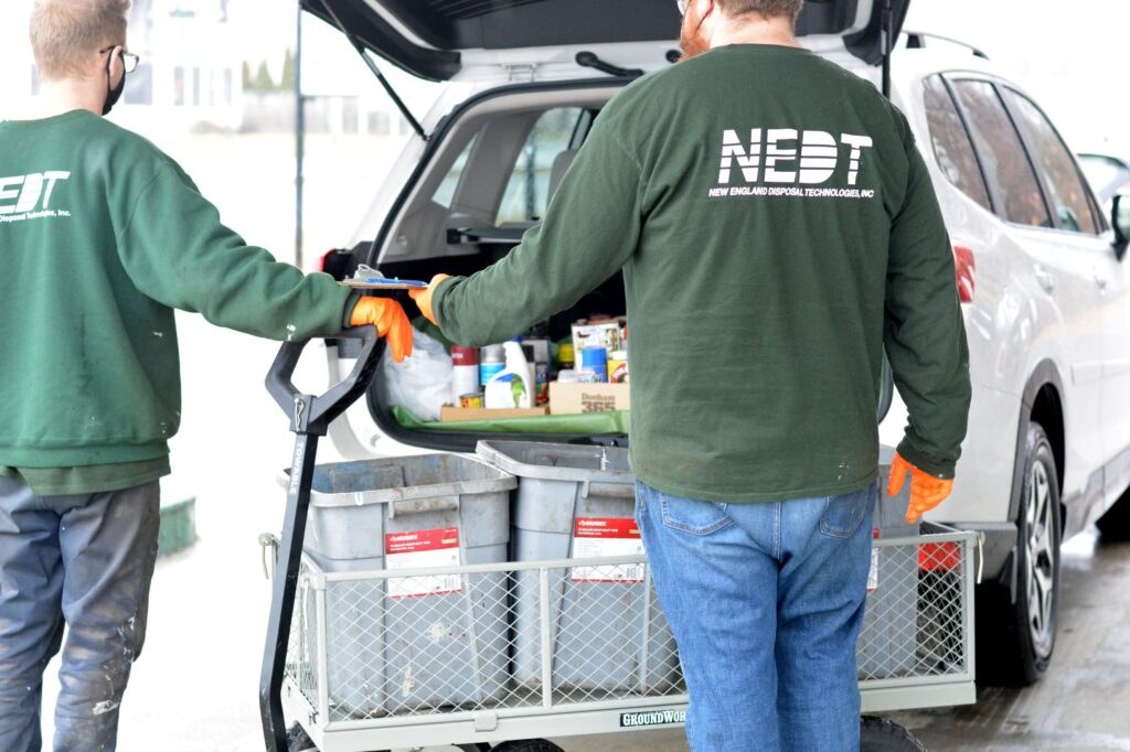 Two NEDT employees stand before an open trunk filled with household hazardous waste.
