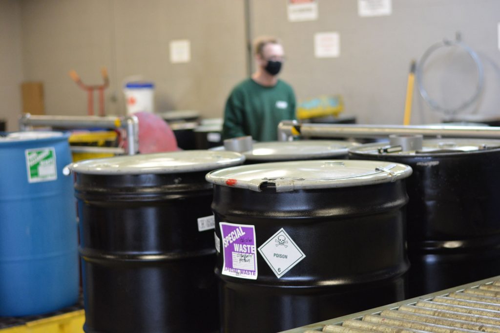 Closeup of hazardous waste containers at an NEDT collection center with employee in background.