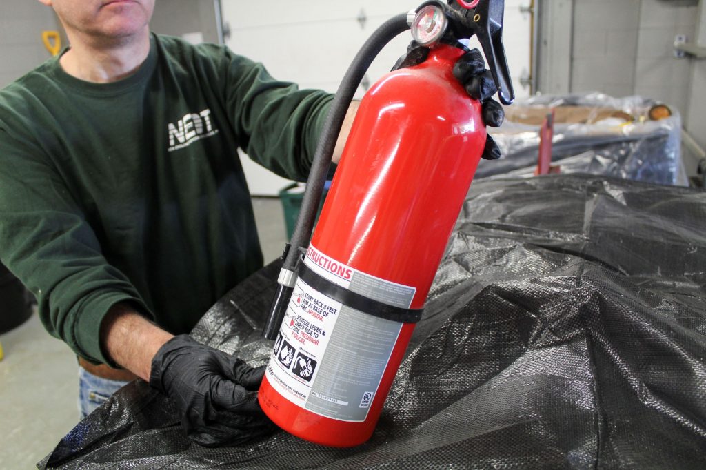 NEDT technician holds an expired fire extinguisher before disposal.