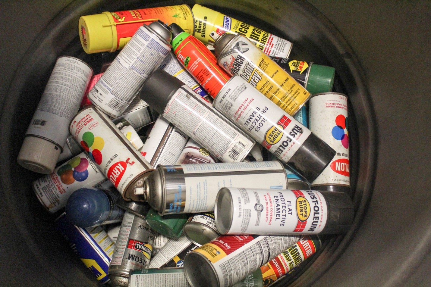 A black bucket full of cans of various colors of spray paint
