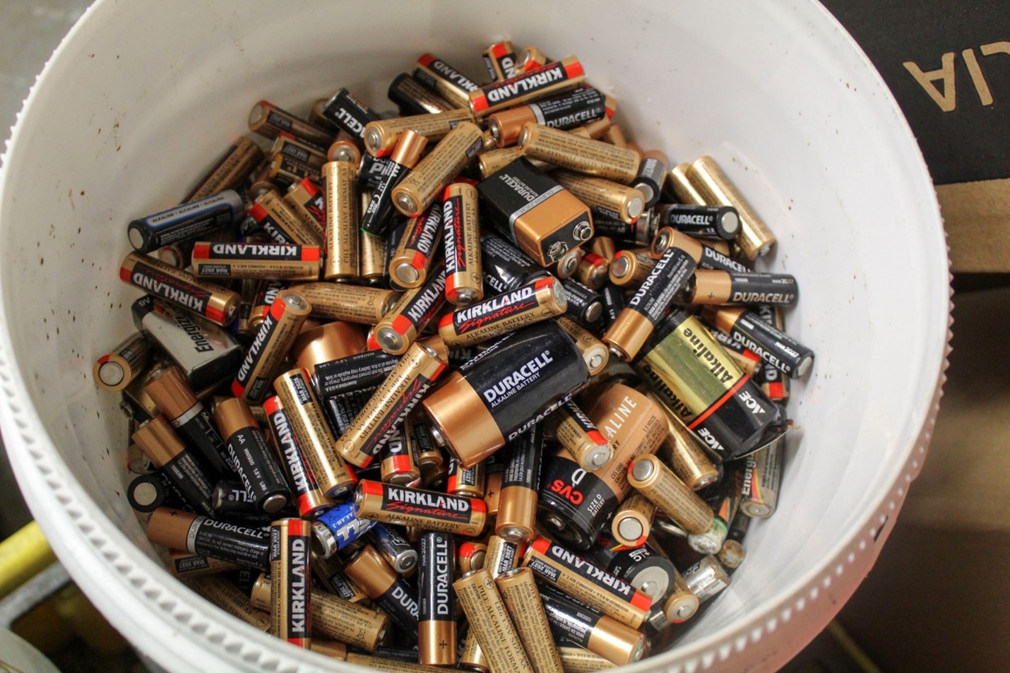 A white bucket ful of an assortment of small batteries
