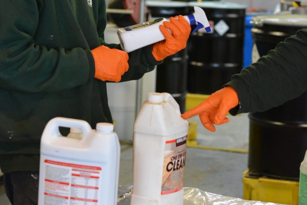 Two orange-gloved NEDT technicians inspect cleaning products before disposal.