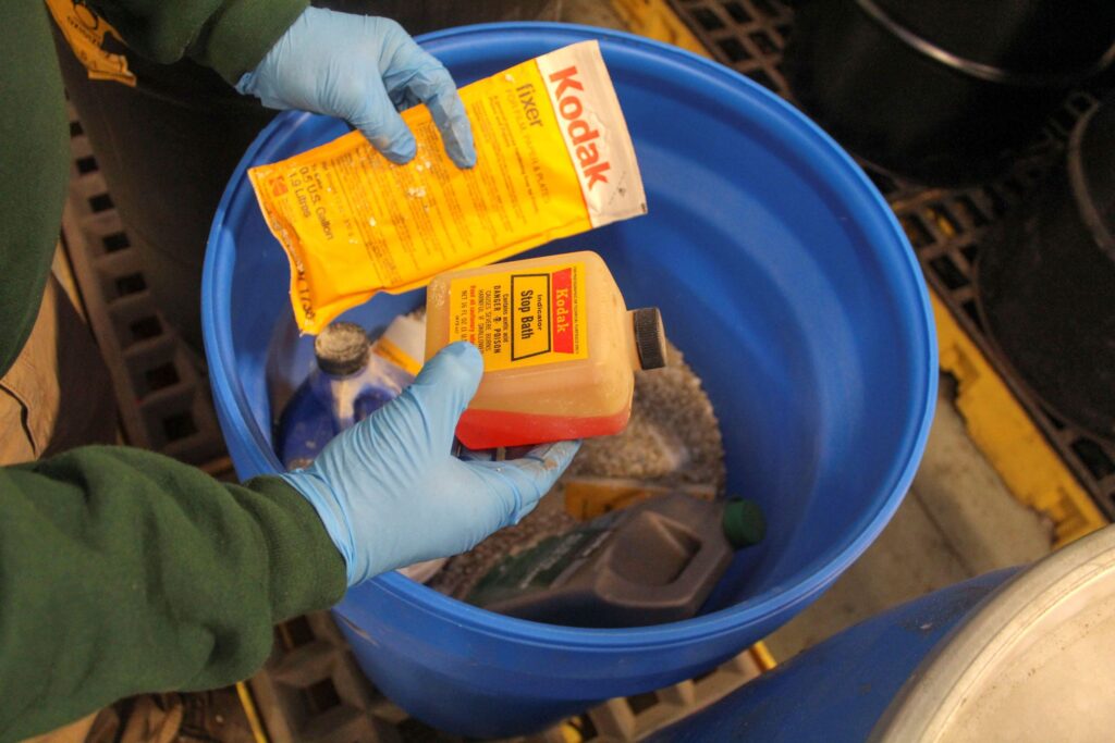 NEDT staffer holds up photograph chemicals, including fixer and stop bath solution.