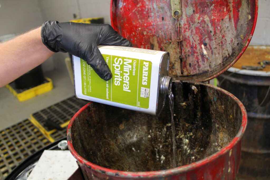 NEDT employee pouring out mineral spirits, a type of paint solvent.