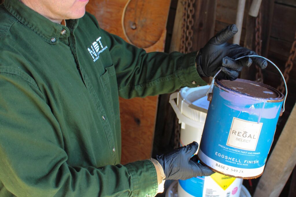NEDT Staffer holds can of latex paint in garage.