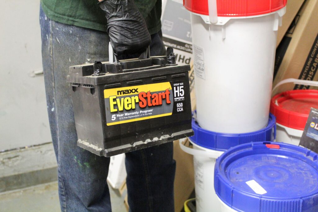 NEDT staff holding an automotive battery for disposal.