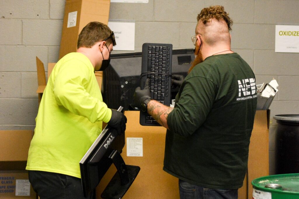 Two NEDT technicians place computer eWaste into a disposal container.
